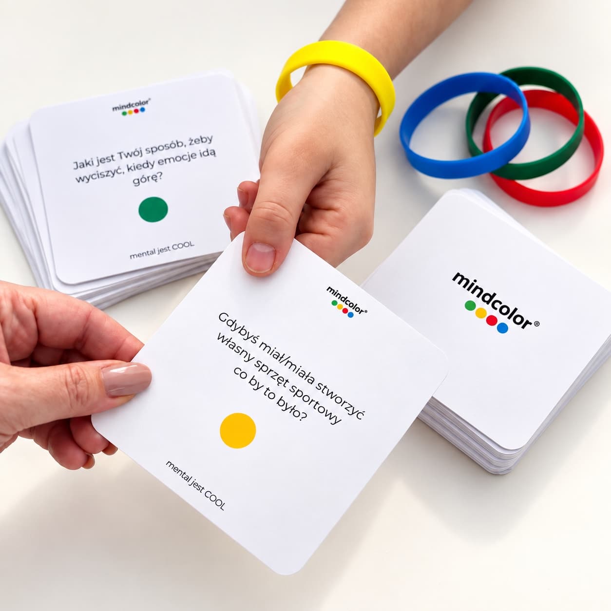 Dłonie wybierające kartę mindcolor® obok kolorowych bransoletek